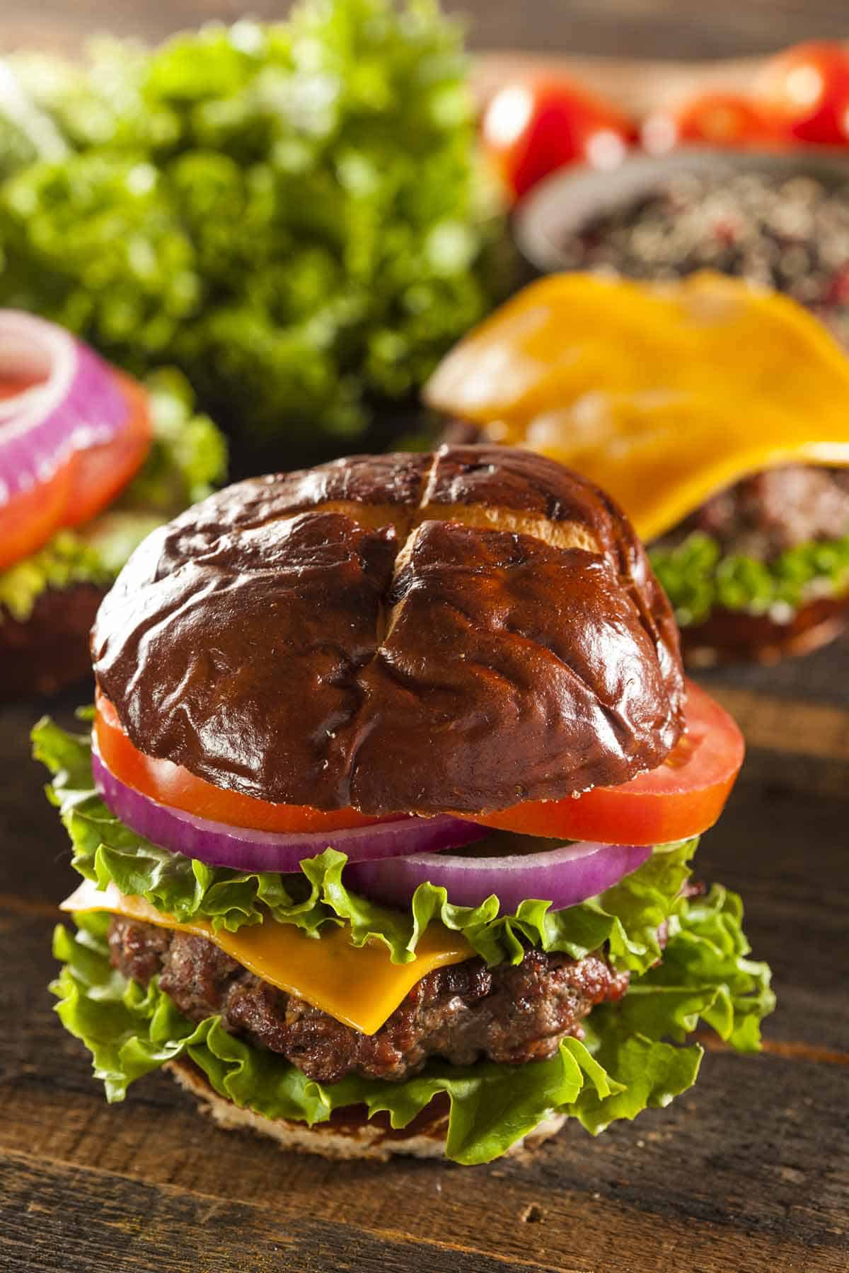 Burger with cheese, lettuce, tomato, and red onions served on a pretzel bun.