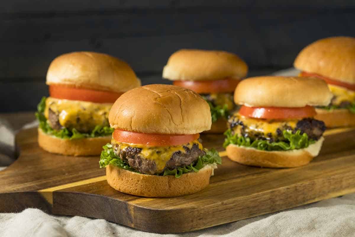 Sandwich board full of slider burgers topped with sliced tomato and lettuce.