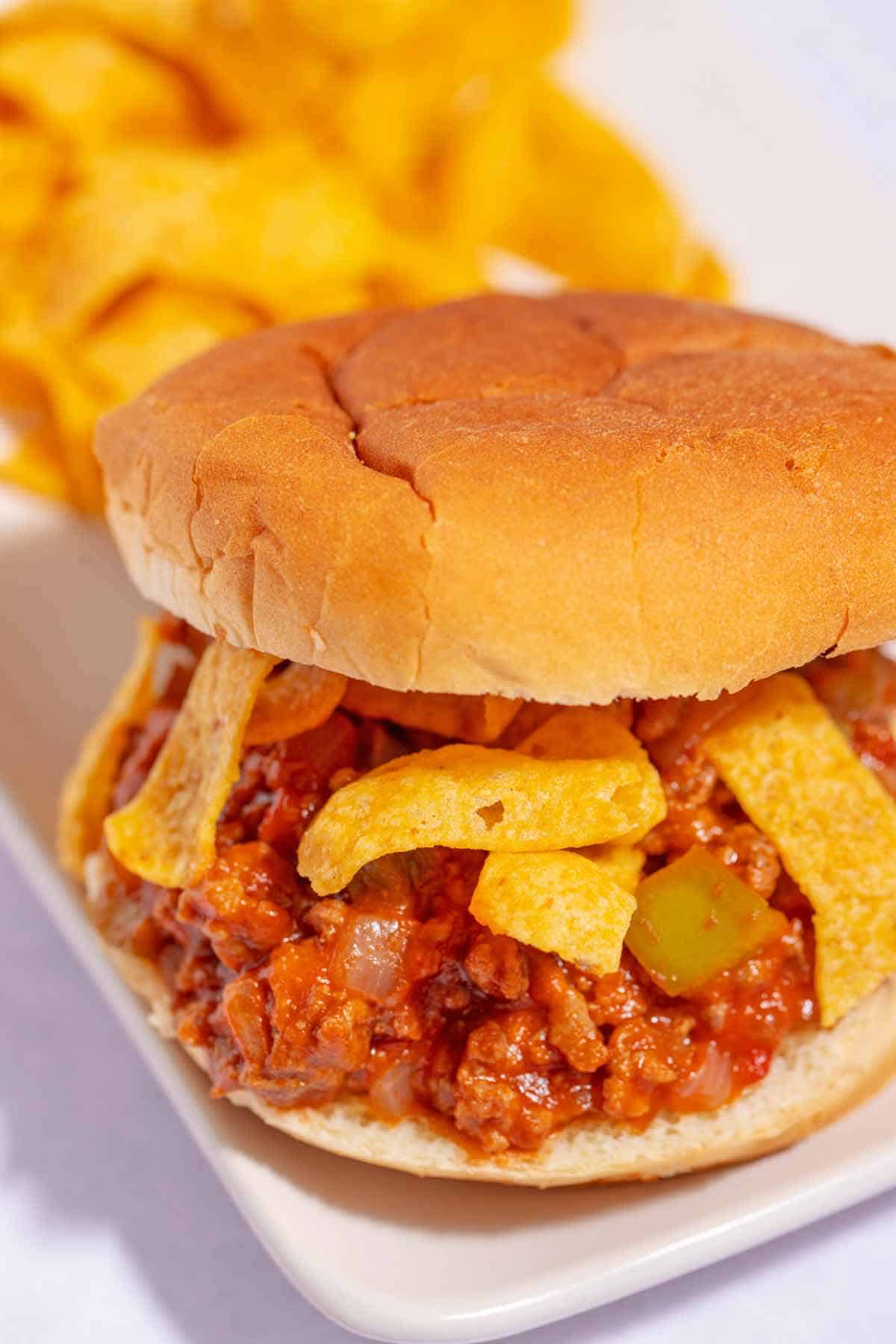 Sloppy joe sandwich on a plain hamburger bun with Frito chips inside the sandwich.