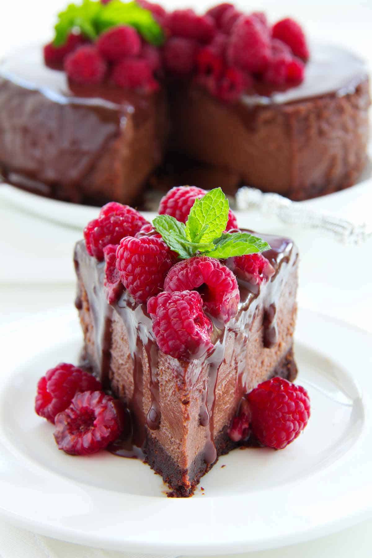 Plate of chocolate raspberry cheesecake with the rest of the cheesecake in the background.