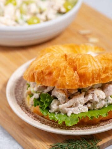 Chicken salad sandwich on a plate with a serving bowl of the salad in the background.