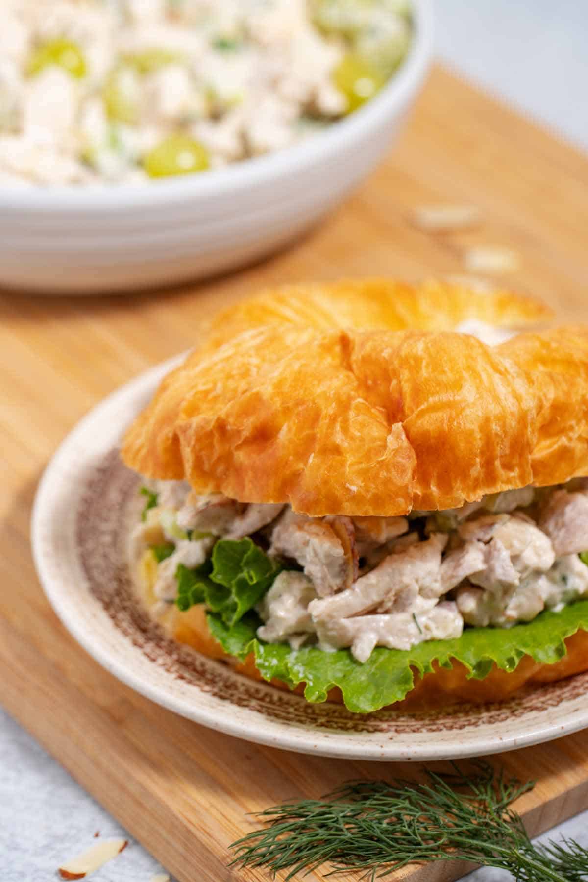 Chicken salad sandwich on a plate with a serving bowl of the salad in the background.
