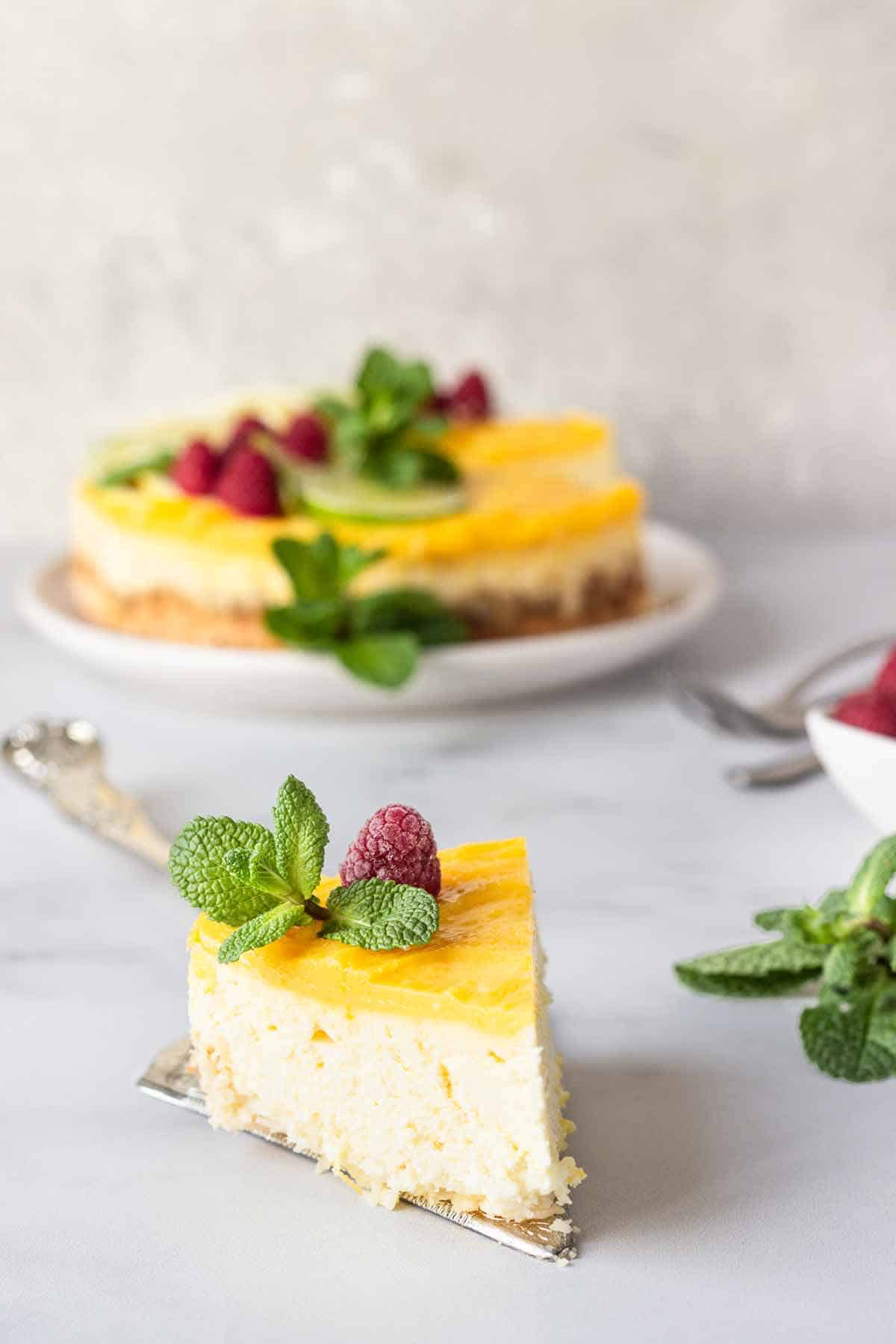 Lemon cheesecake on a serving spoon with the rest of the cheesecake in the background.