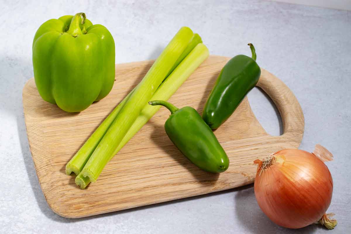 Cutting board with green bell pepper, celery, jalapeno peppers, and yellow onion.