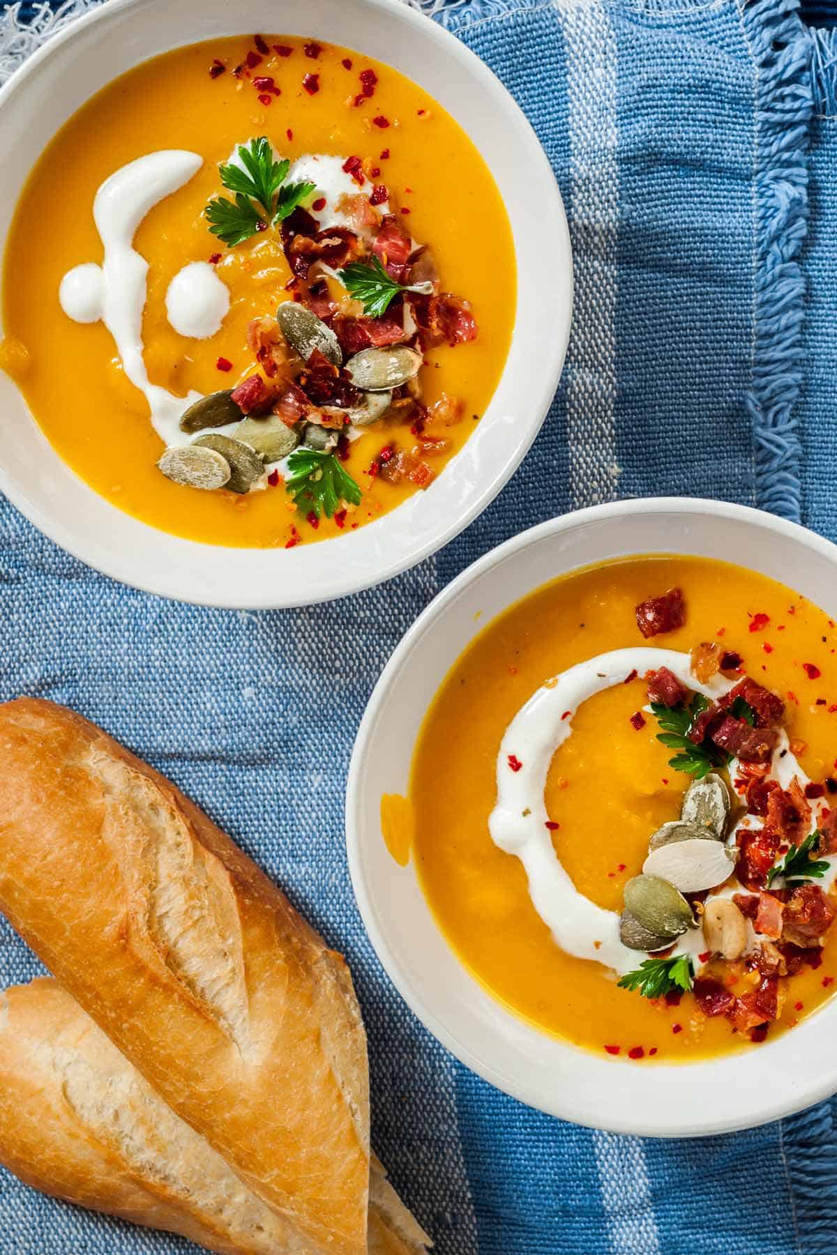 Two bowls of butternut squash soup with crusty bread on the side.