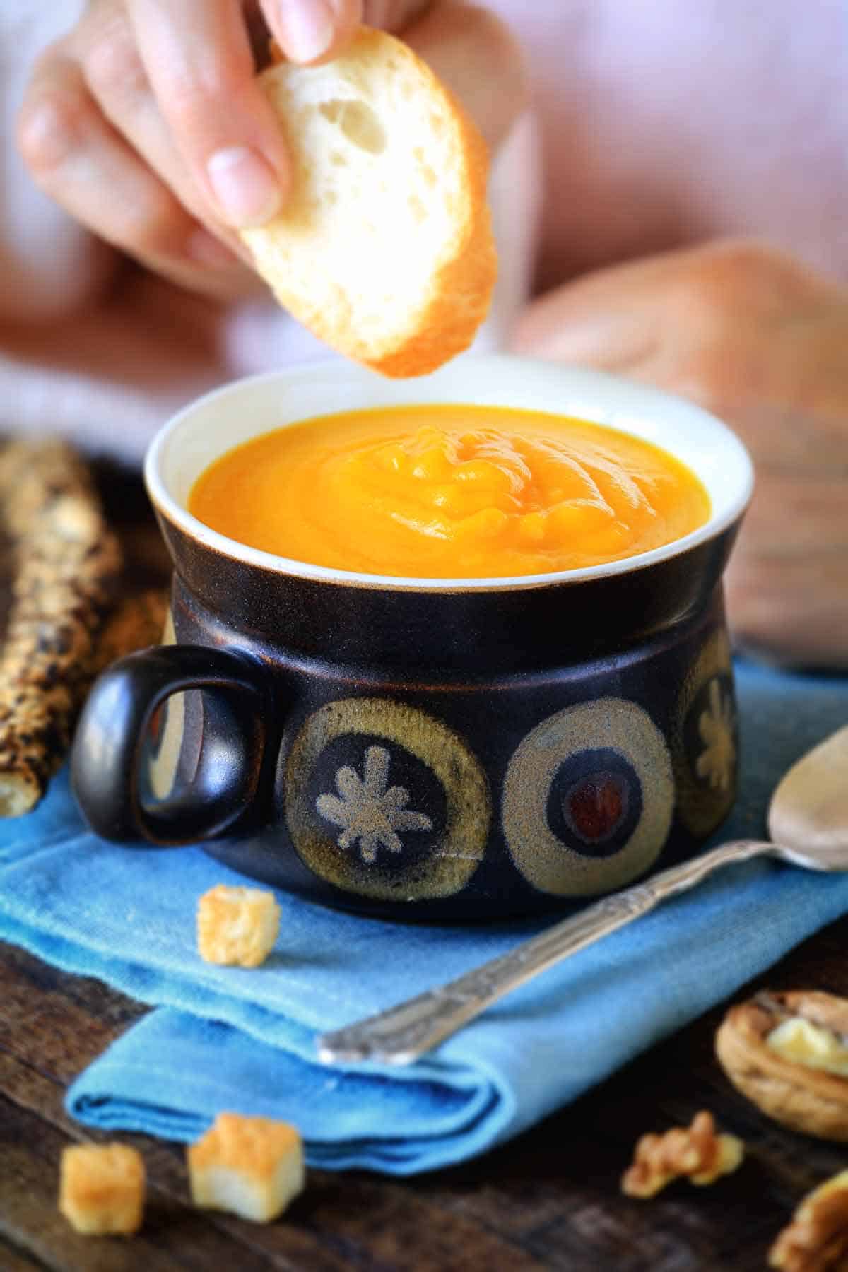 Dunking a piece of crusty bread in a bowl of pumpkin soup.