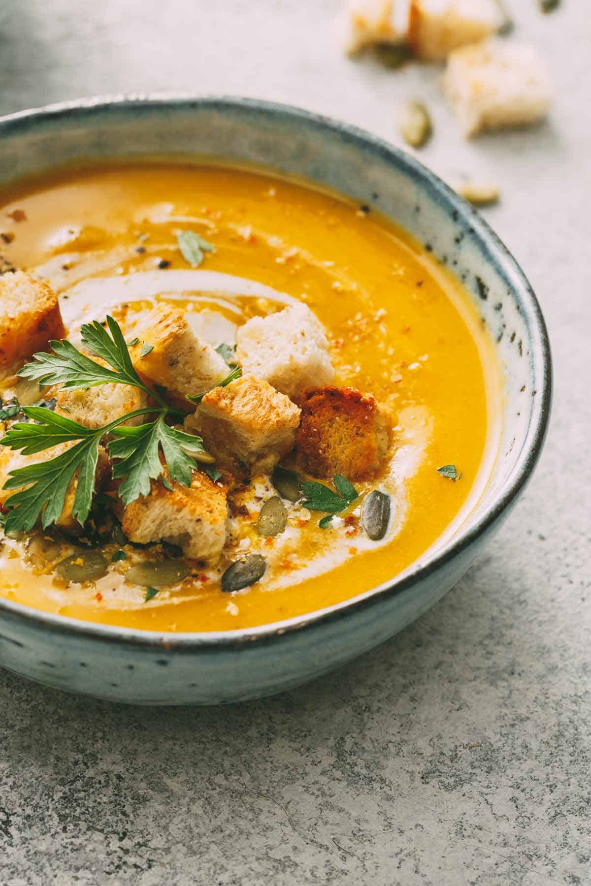 Bowl of pumpkin soup with the best toppings (croutons, parsley, pepitas, and cream).