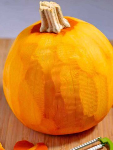 Whole raw peeled pumpkin on a cutting board.
