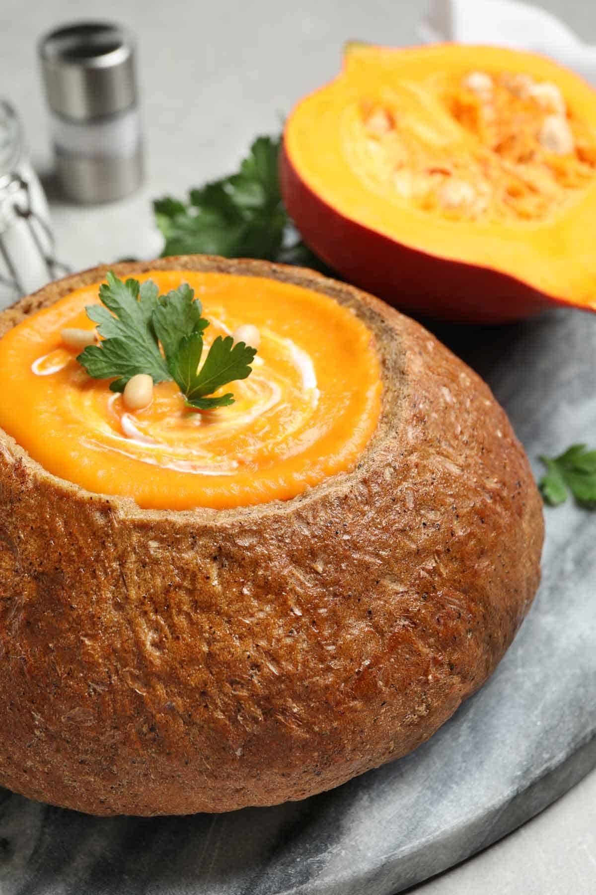 Bread bowl filled with pumpkin soup and garnished with parsley and pine nuts.