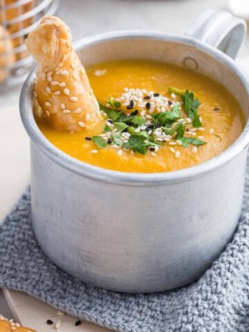 Cup of butternut squash soup with breadstick dipped in.