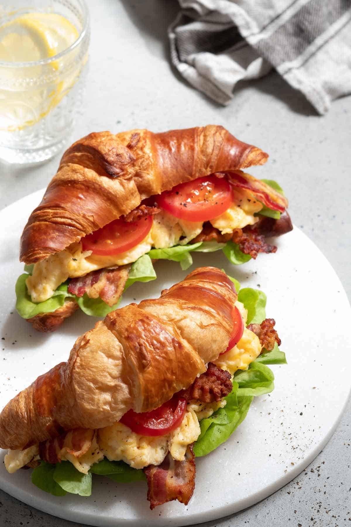Egg, tomato, and bacon croissant sandwich on a serving tray.