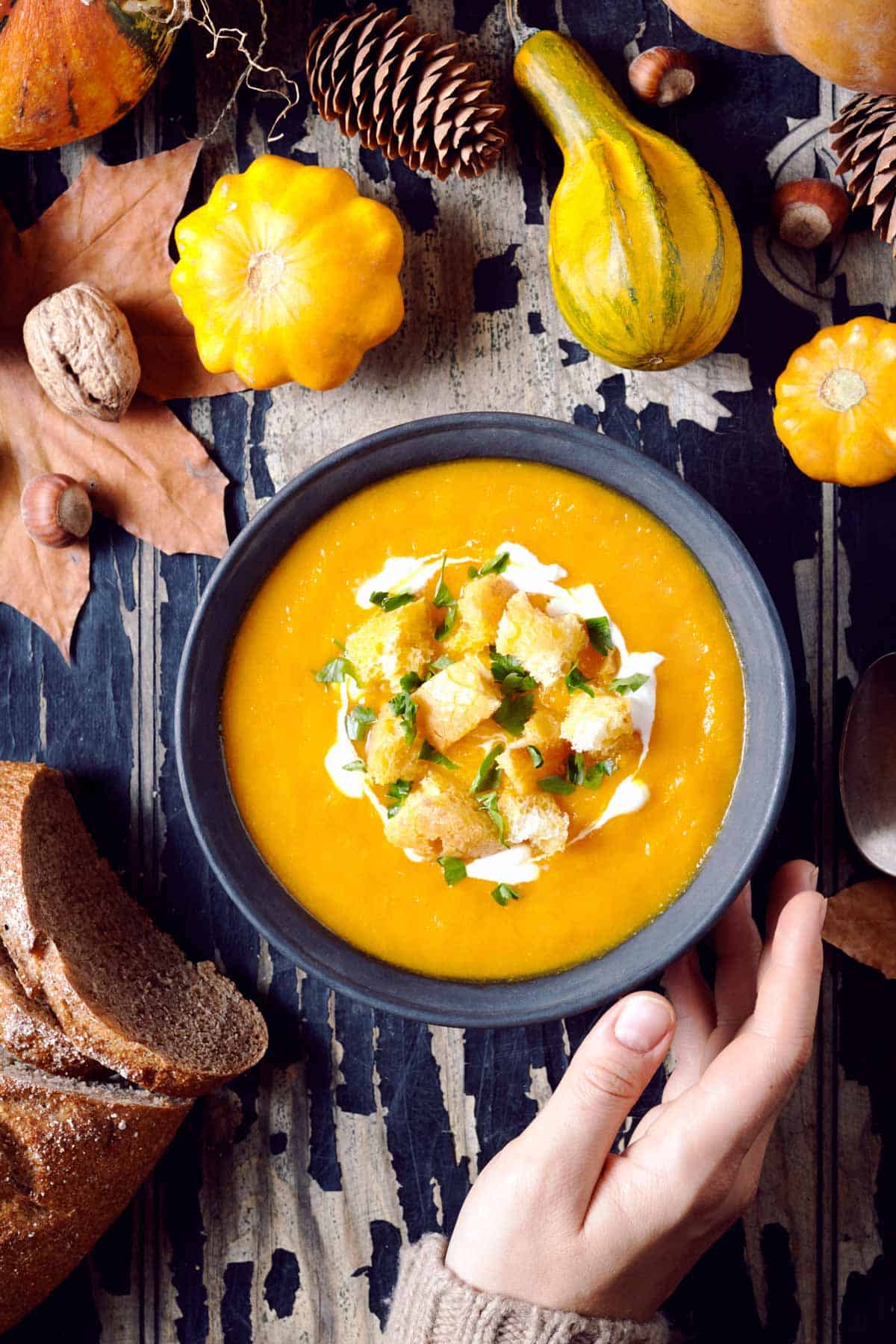 Bowl of thick pumpkin soup garnished with croutons, chives, and cream.