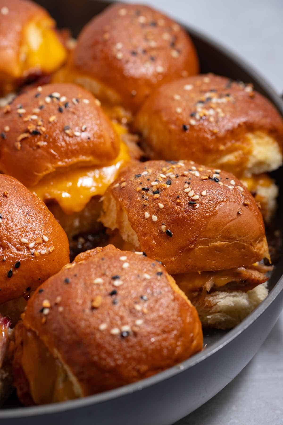 Pan of pulled pork sliders with cheddar cheese and pickled jalapeno peppers.