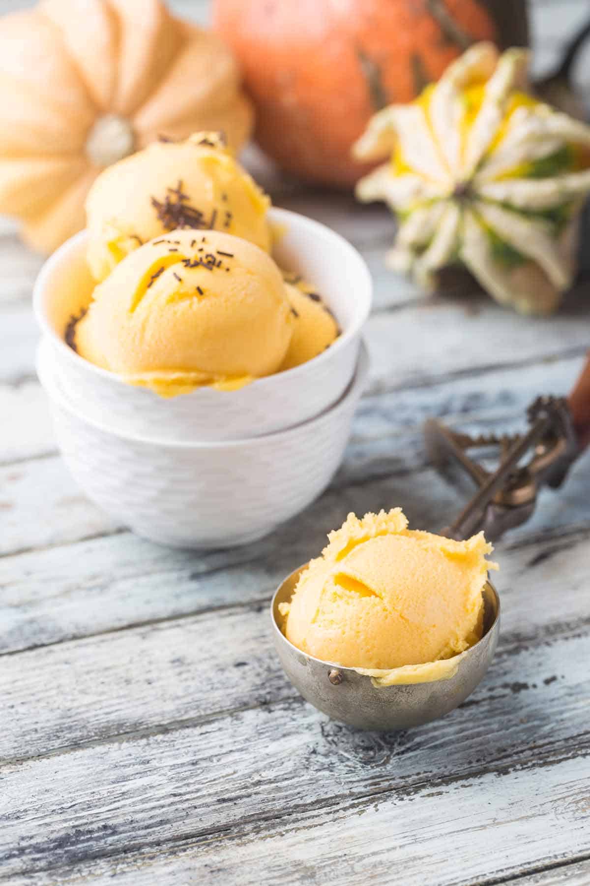 Scoop of pumpkin ice cream with a bowl of ice cream in the background.