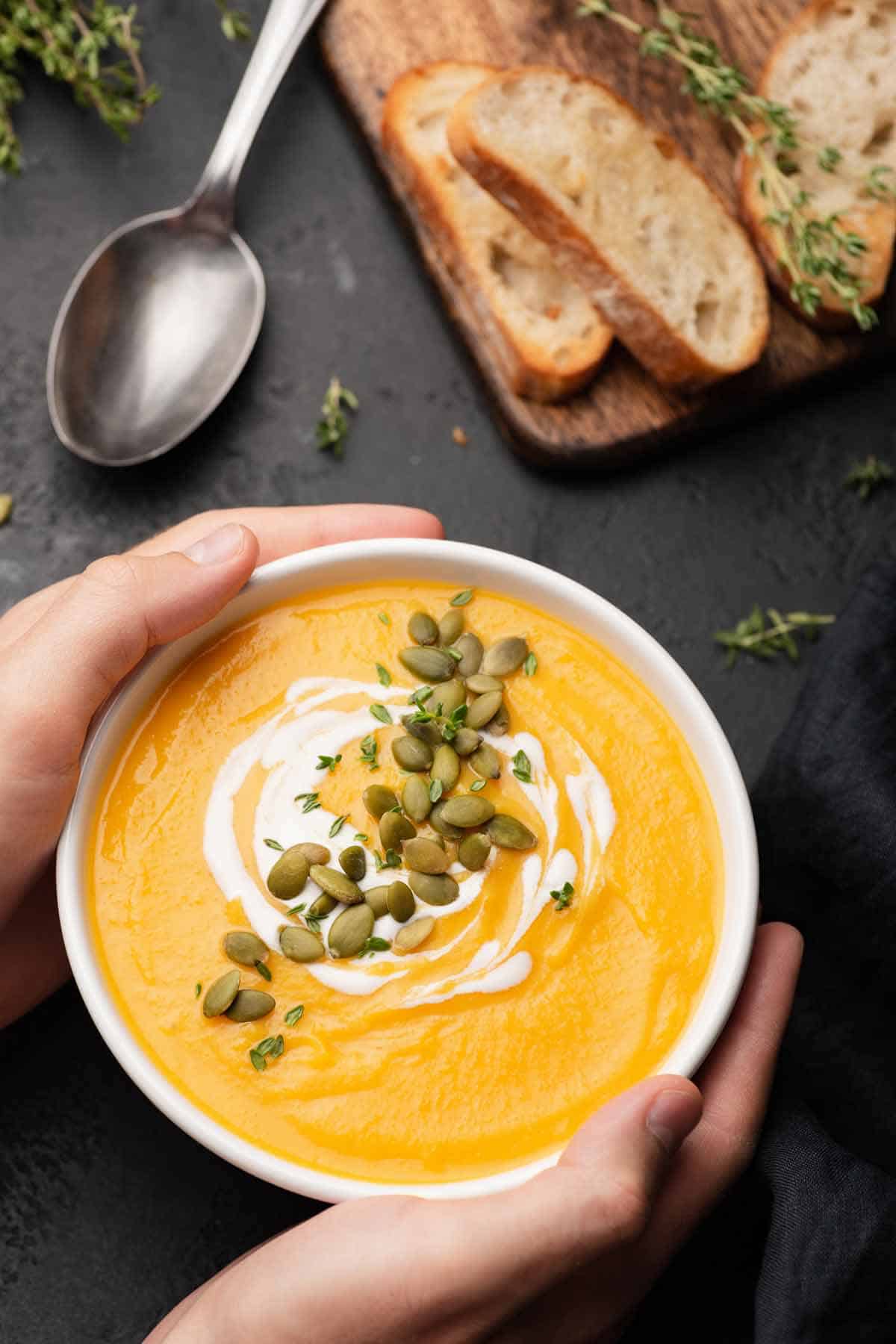 Bowl of pumpkin soup garnished with pepitas, thyme, and cream.