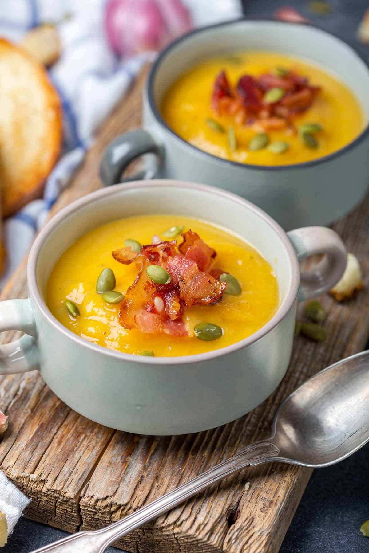 Two bowls of pumpkin soup garnished with crisp bacon.