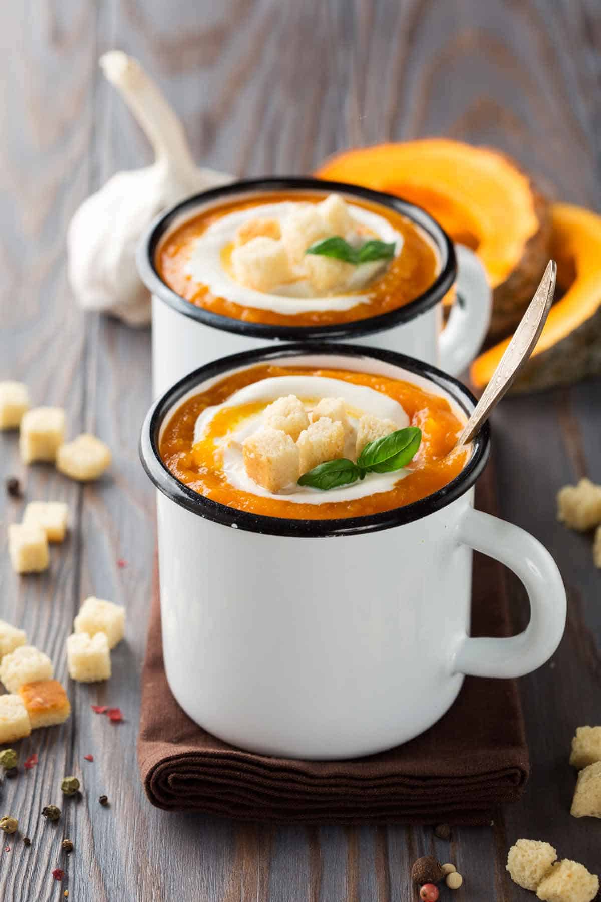 Two mugs of pumpkin soup garnished with croutons.
