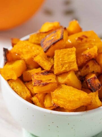 Bowl of roasted pumpkin cubes with whole pumpkin in the background.