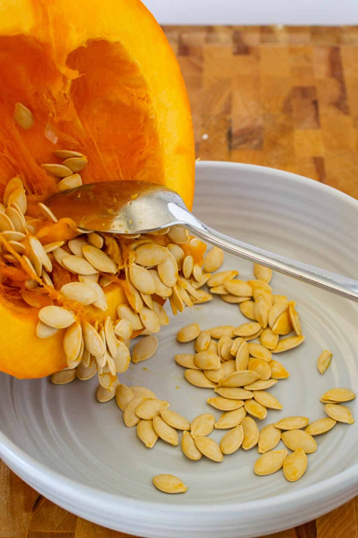 Spoon scraping out the pumpkin seeds and string into a bowl.