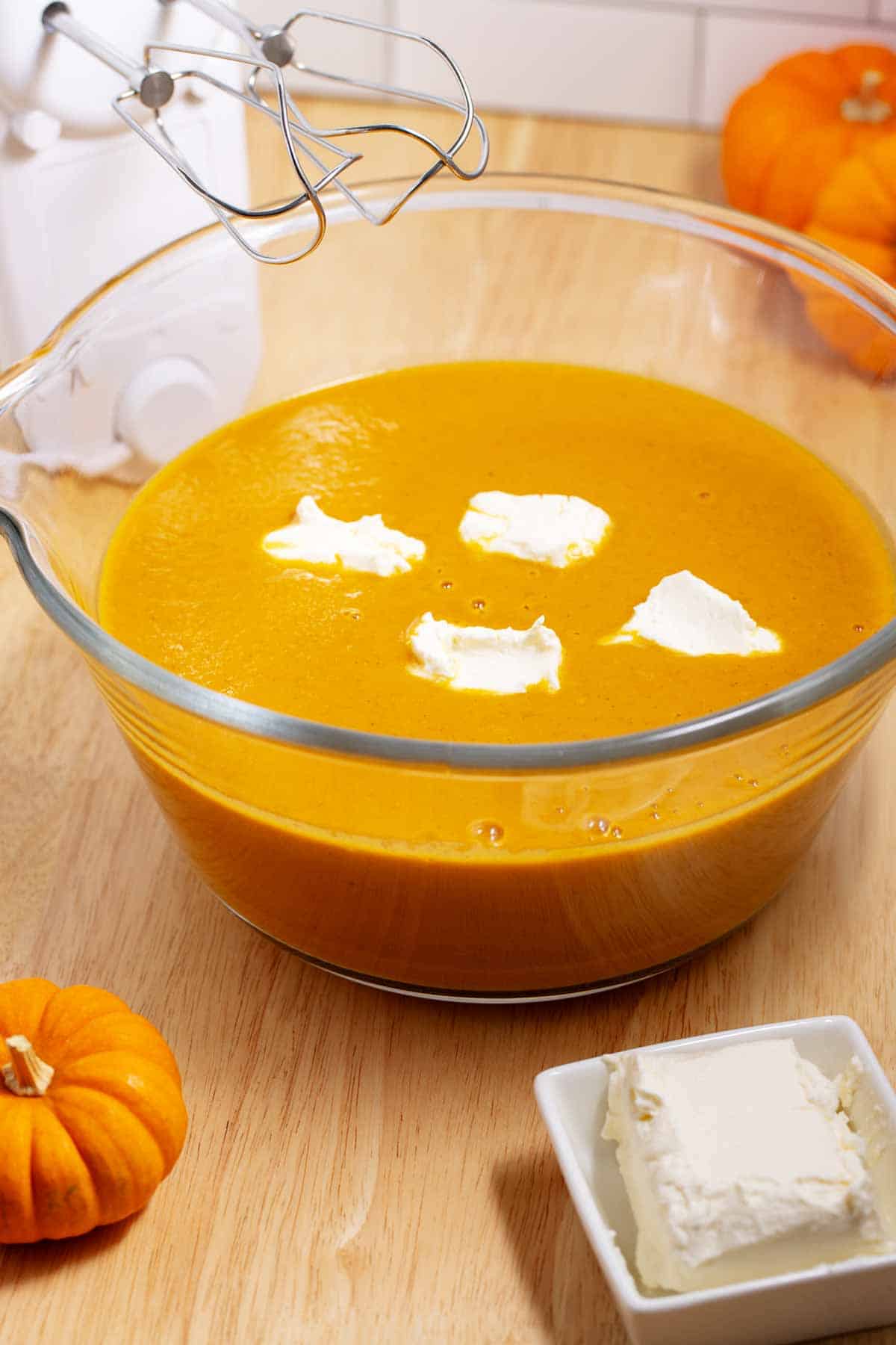 A mixing bowl of pumpkin soup with cream cheese added and ready to be whipped to thicken the soup.