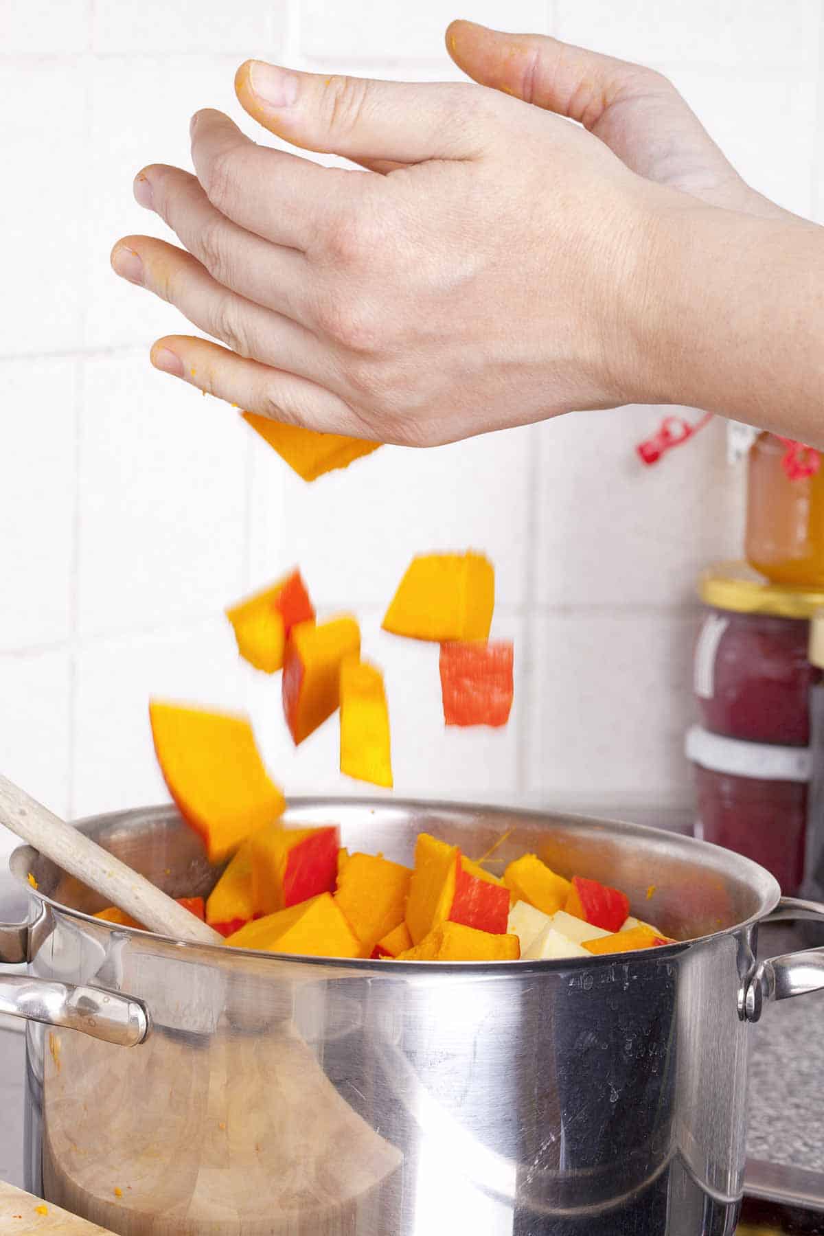 Hands dropping raw pumpkin into the soup pot.