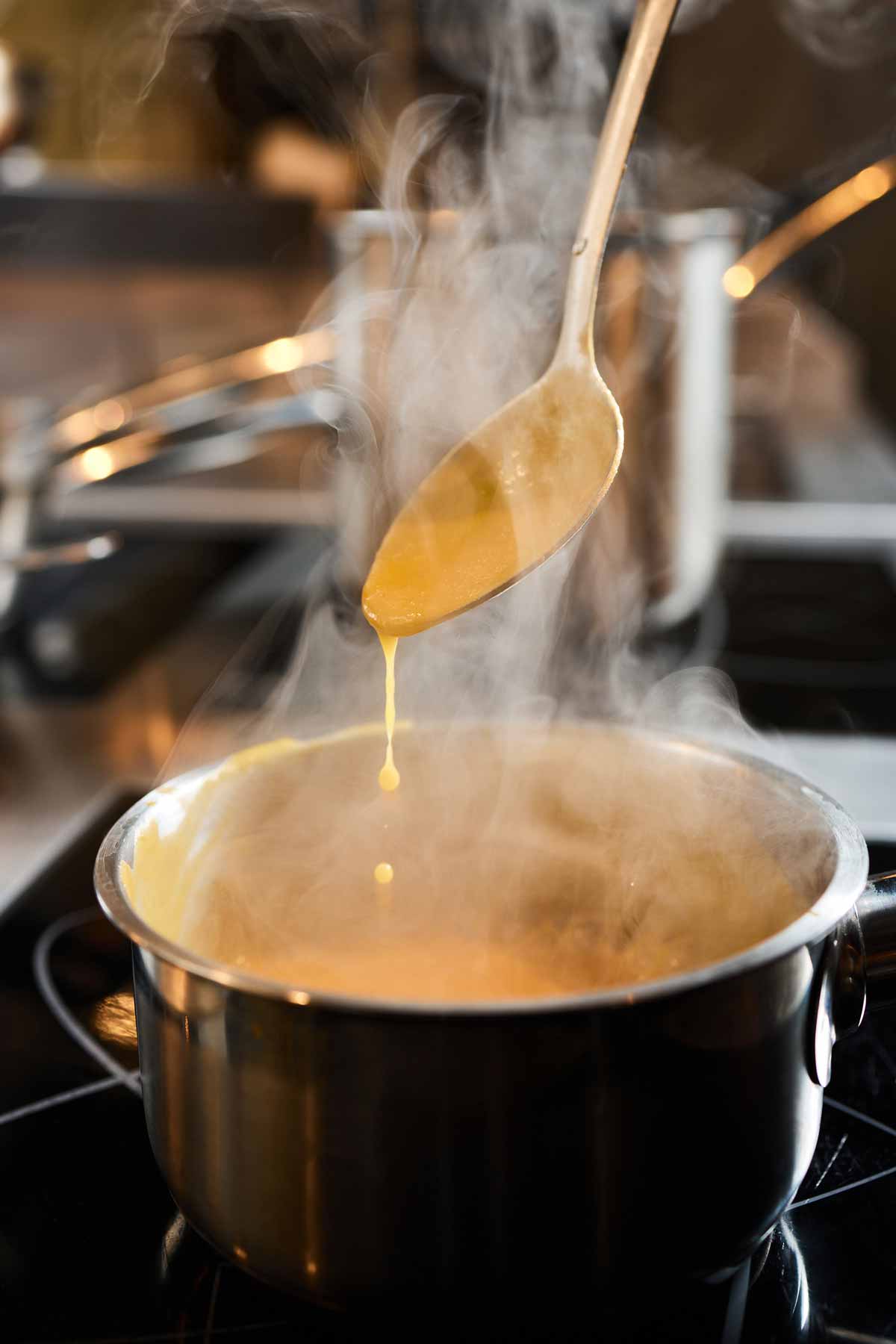 Pan of pumpkin soup simmering on the stove, being thickened by reduction.