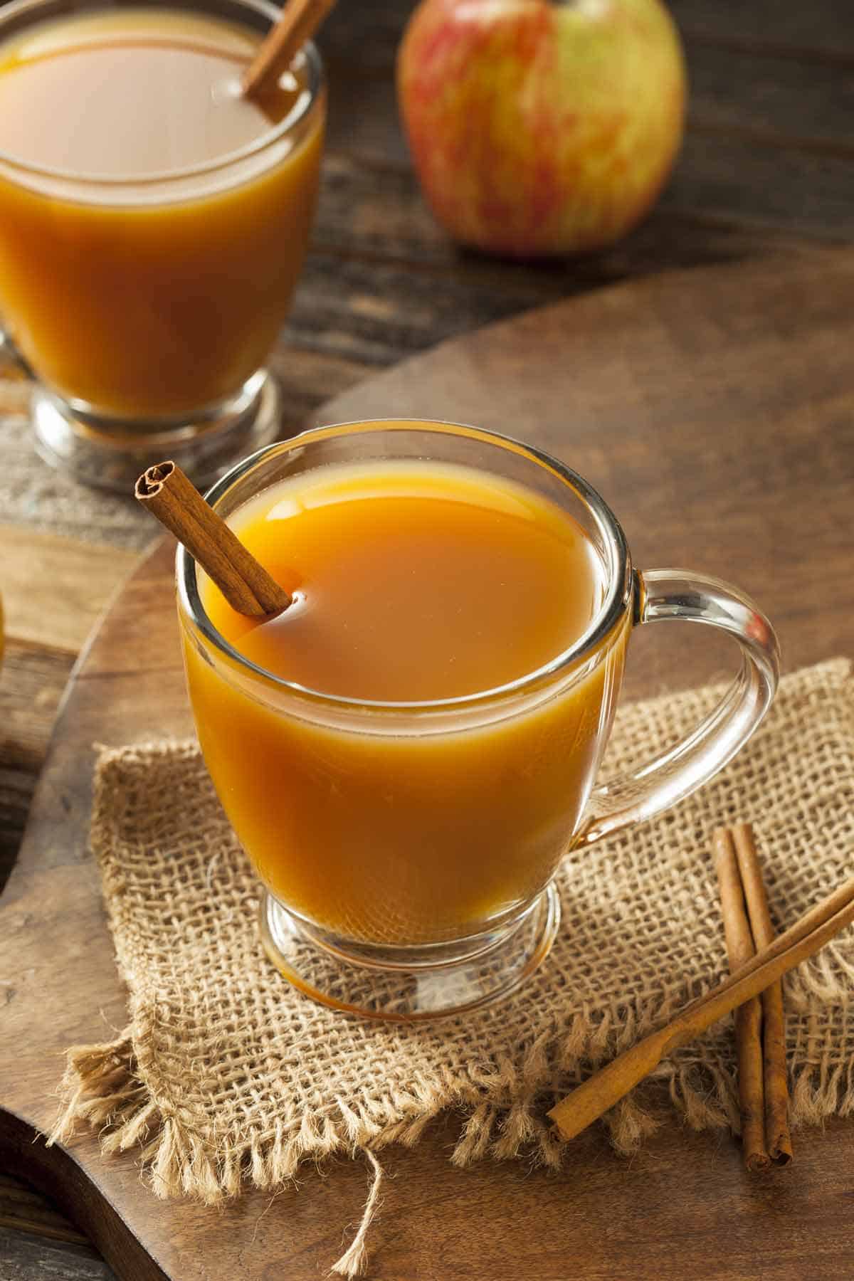 Two glasses of hot apple cider with a cinnamon stick.