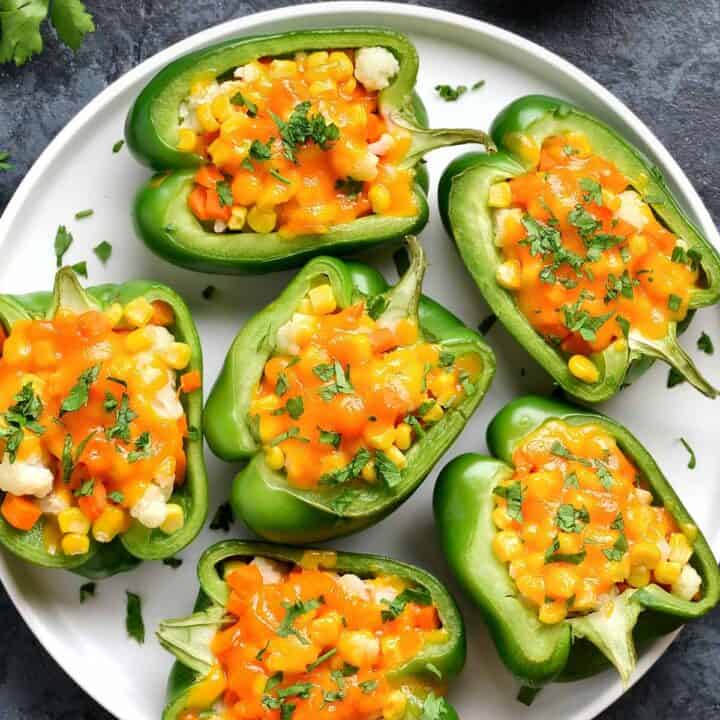 Plate of green bell pepper sandwiches, filled with veggies. Bowl of creamy dip is at the side.