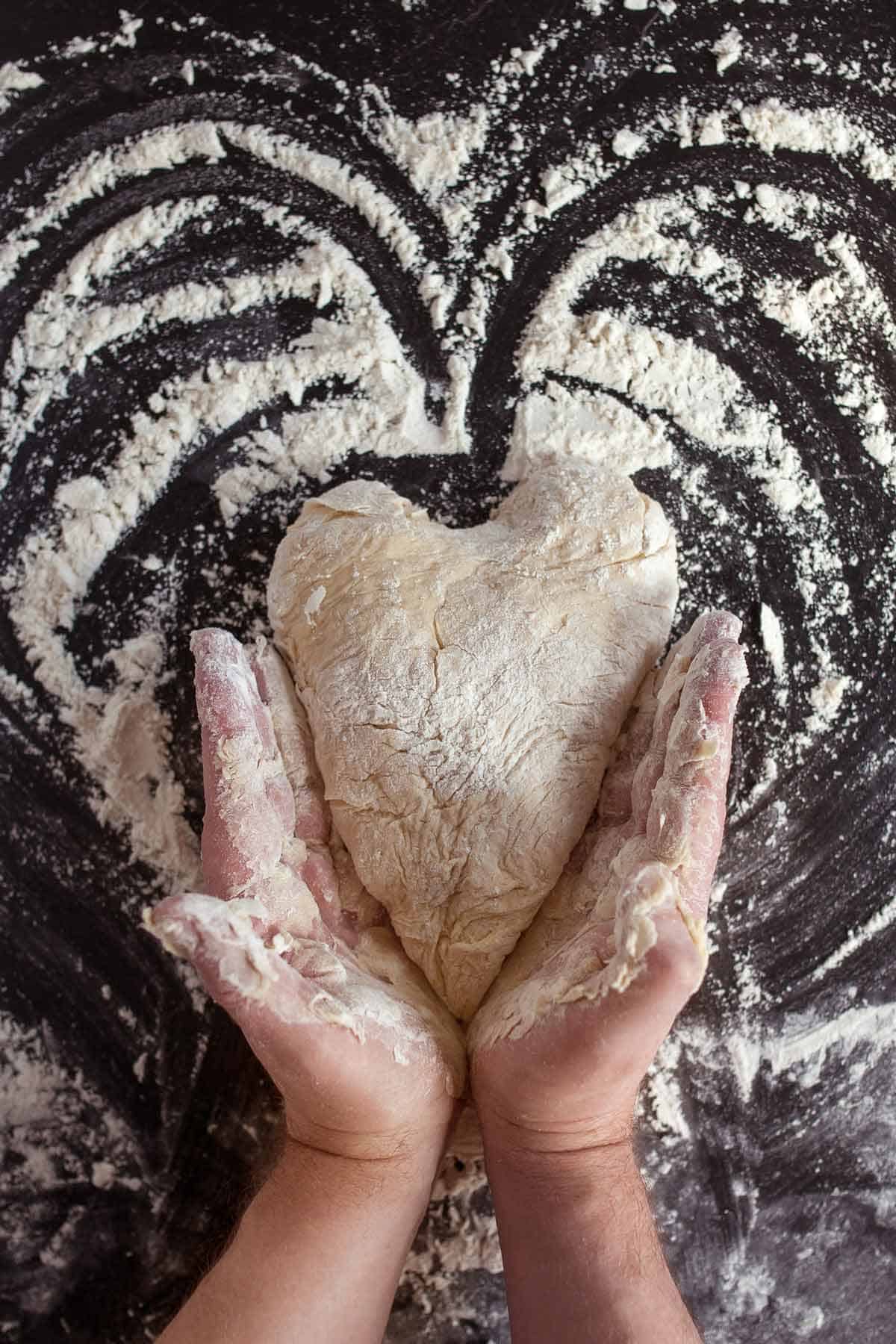 Hands shaping pizza dough into a heart shape.