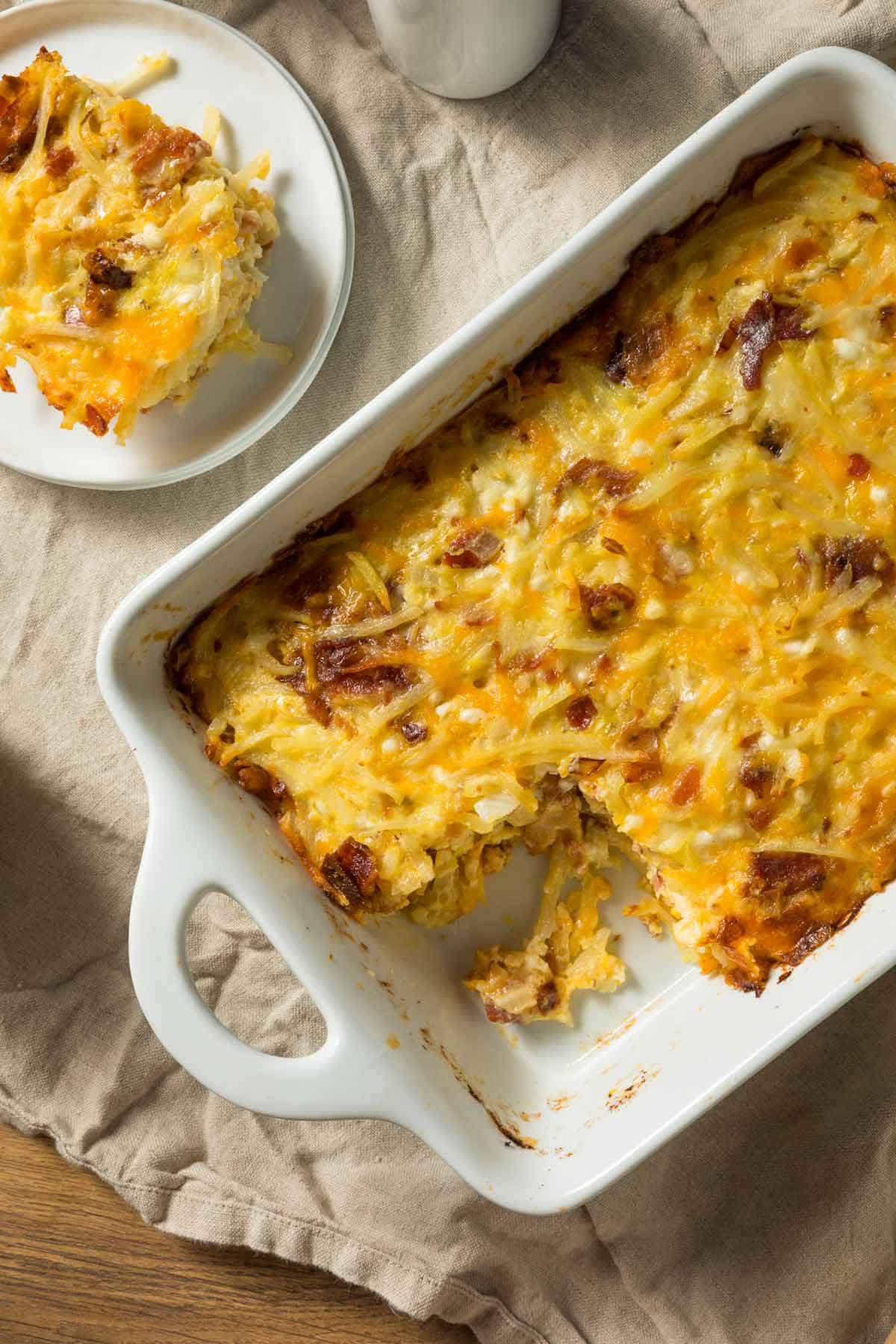 Breakfast casserole in a casserole pan with a serving of the casserole on a small plate in the background.