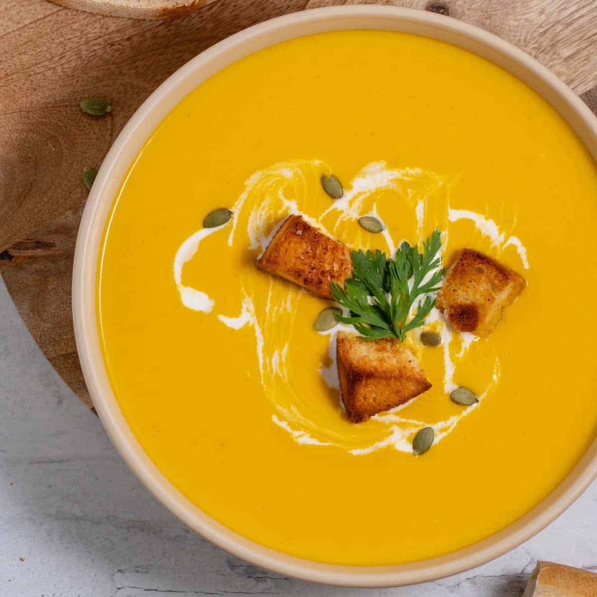 Bowl of butternut squash soup with cream cheese, garnished with croutons.