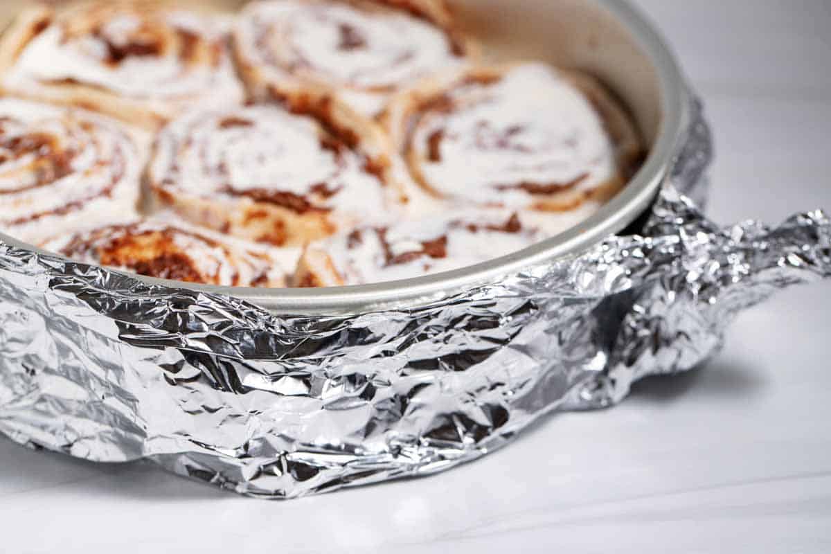 Closeup of homemade cake strips around a cake pan full of unbaked canned cinnamon rolls.