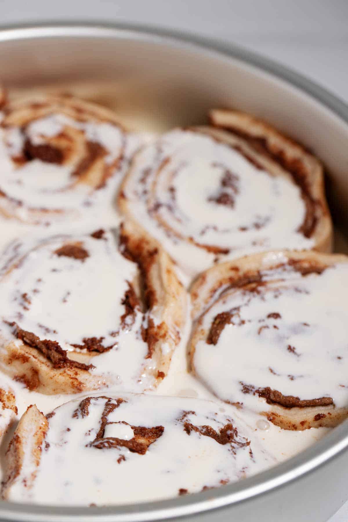 Pan of unbaked canned cinnamon rolls drenched in cream.