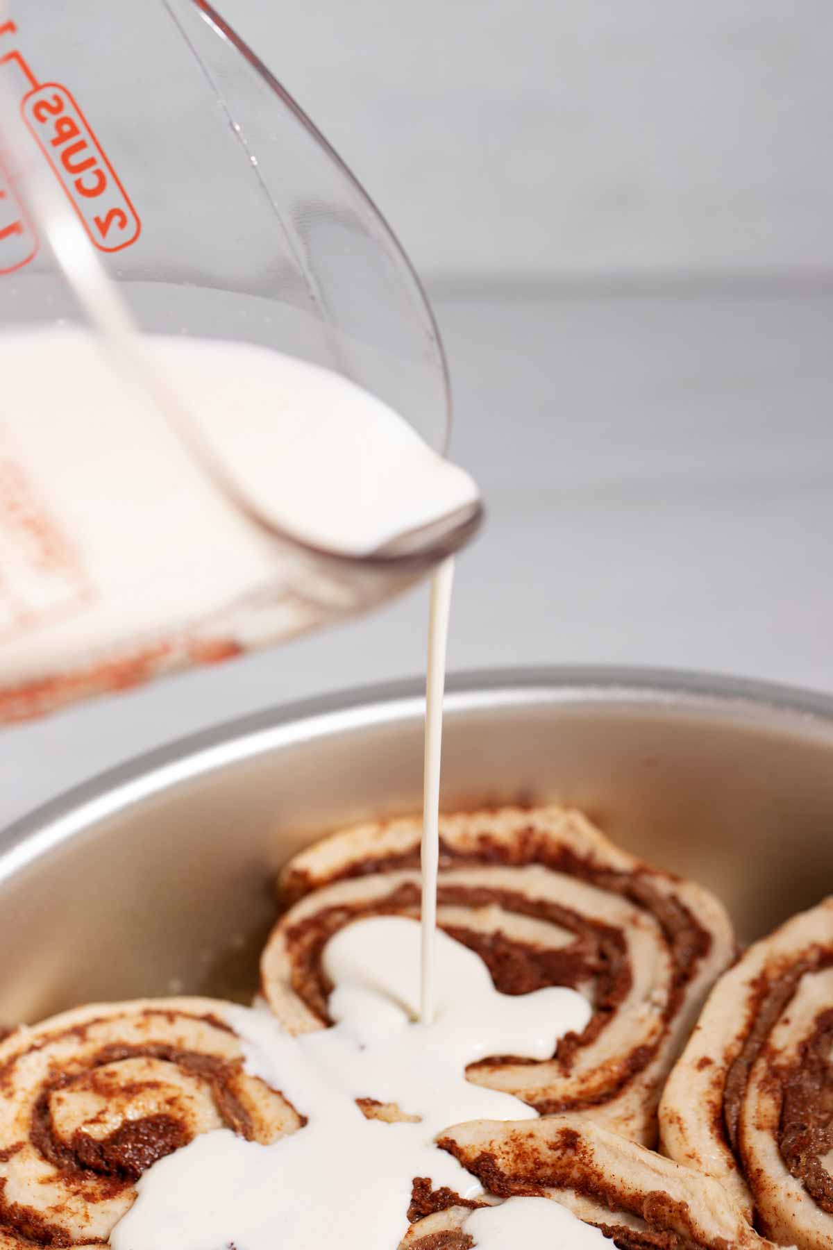 Pouring cream on unbaked canned cinnamon rolls in a pan.