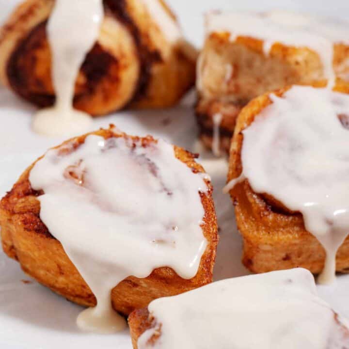 A batch of baked cinnamon rolls with fresh cream cheese frosting dripping on the top and down the sides of the rolls.