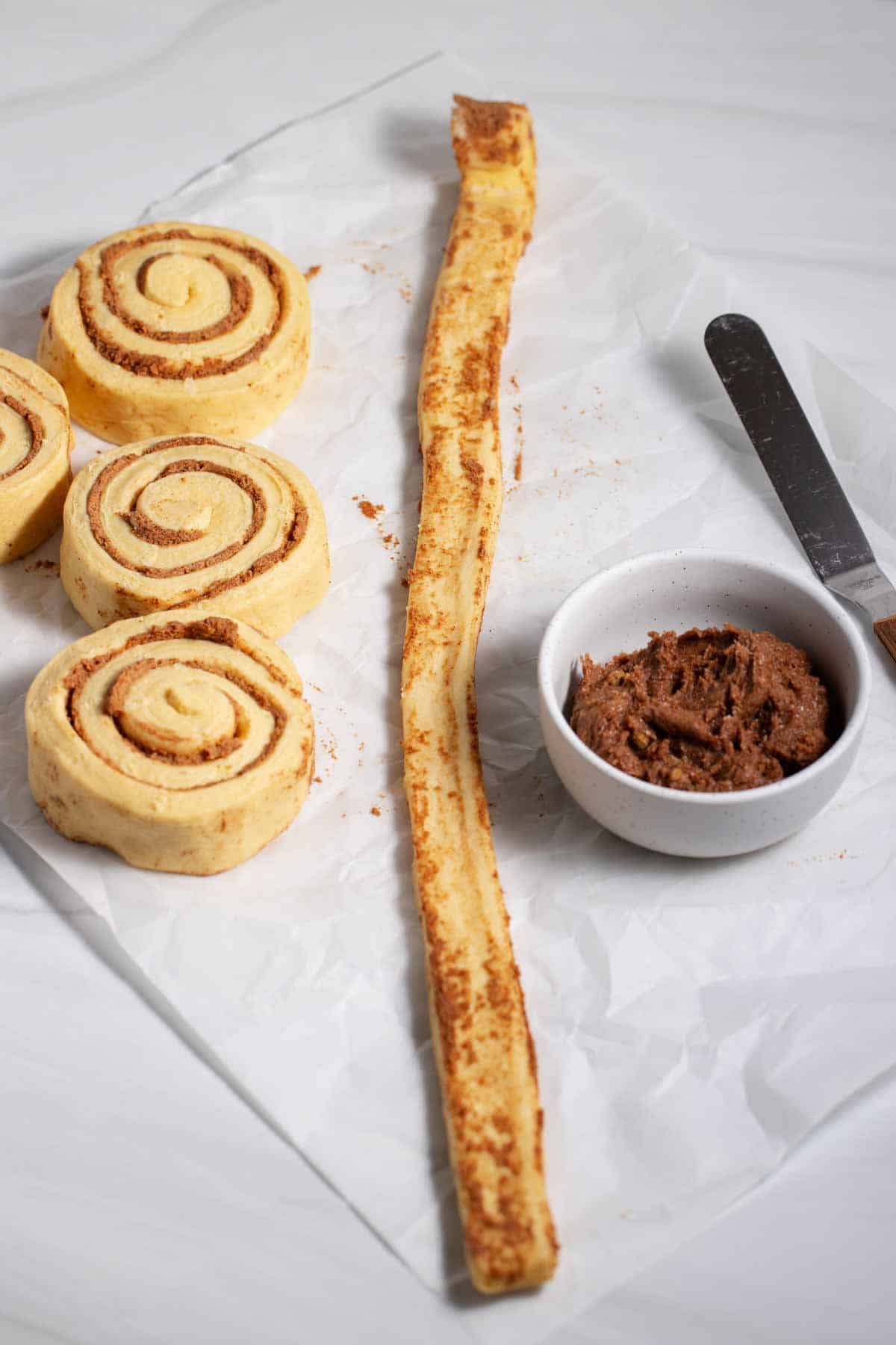 Unrolled cinnamon roll with bowl of butter, brown sugar, and cinnamon mixture.