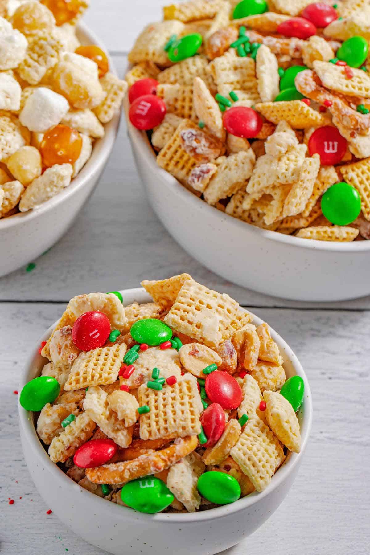 Bowl of Christmas Chex mix with larger serving bowls behind it.