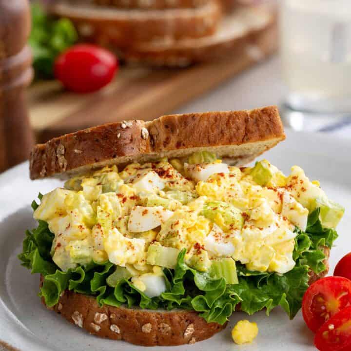 Egg salad sandwich with lettuce on a plate with halved cherry tomatoes.