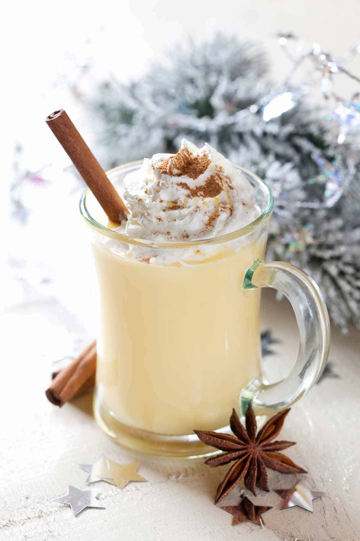 Glass on eggnog with whipped cream and a cinnamon stick.