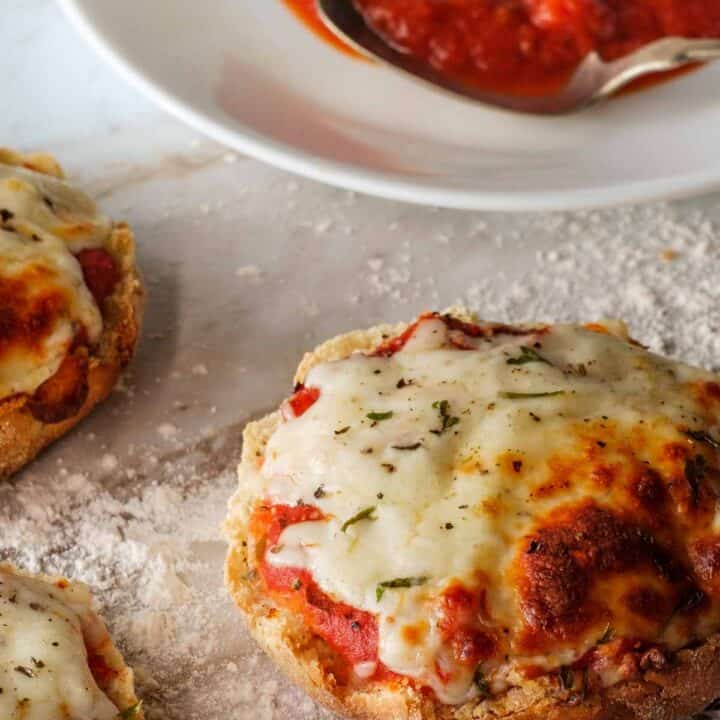 English muffins pizza with pizza sauce in the background.
