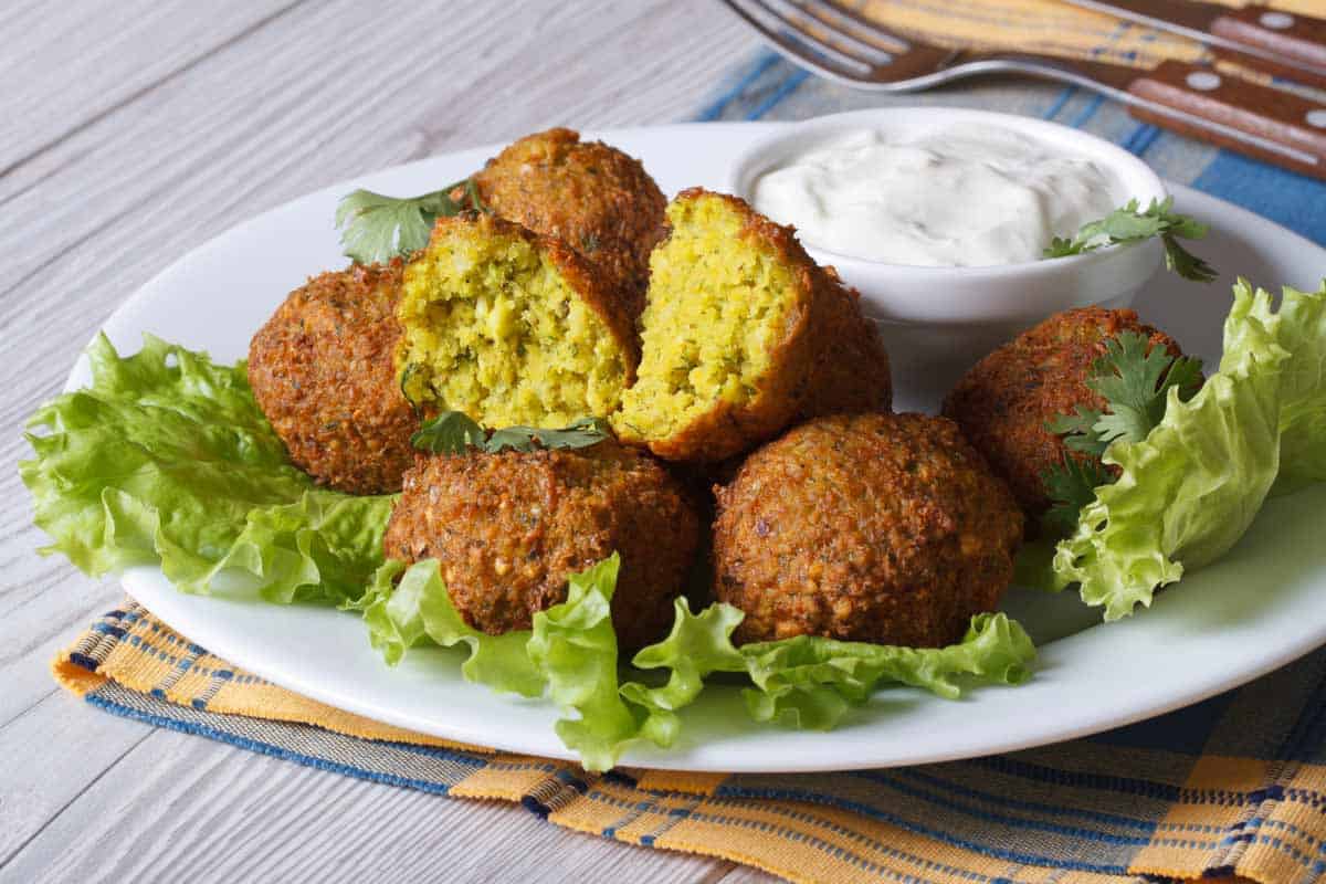 Plate of falafel on a bed of lettuce with a bowl of dip.