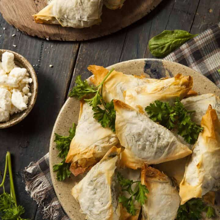 Feta and spinach triangles on a plate with parsley as a garnish.