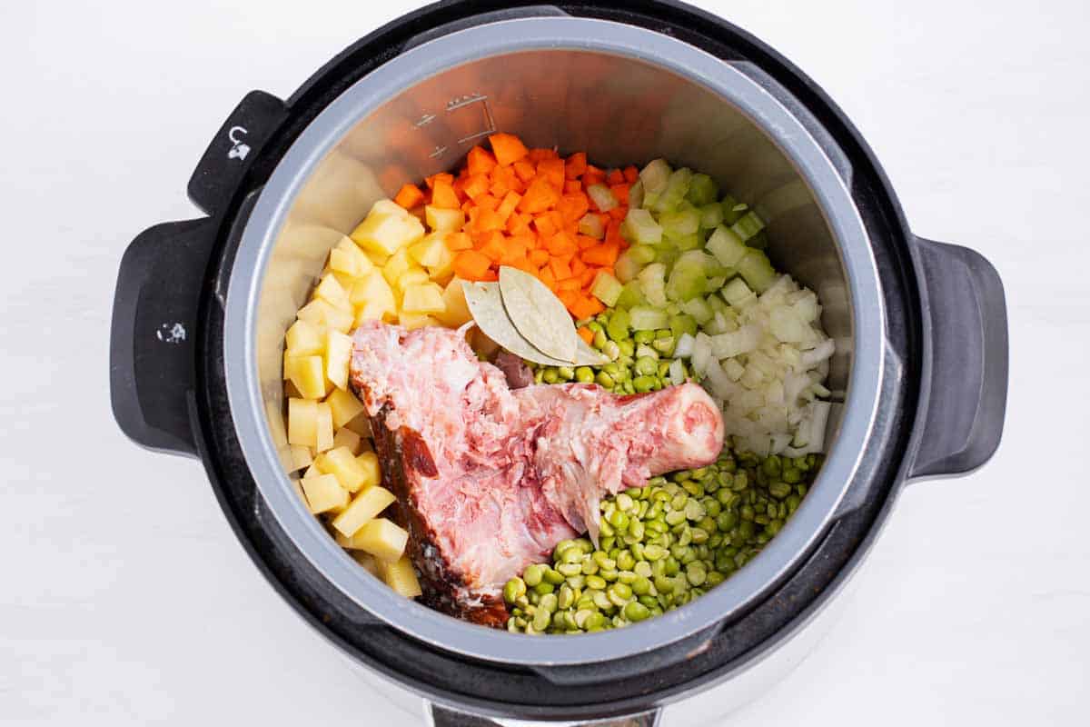 Ingredients for split pea soup in a pressure cooker with ham bone.