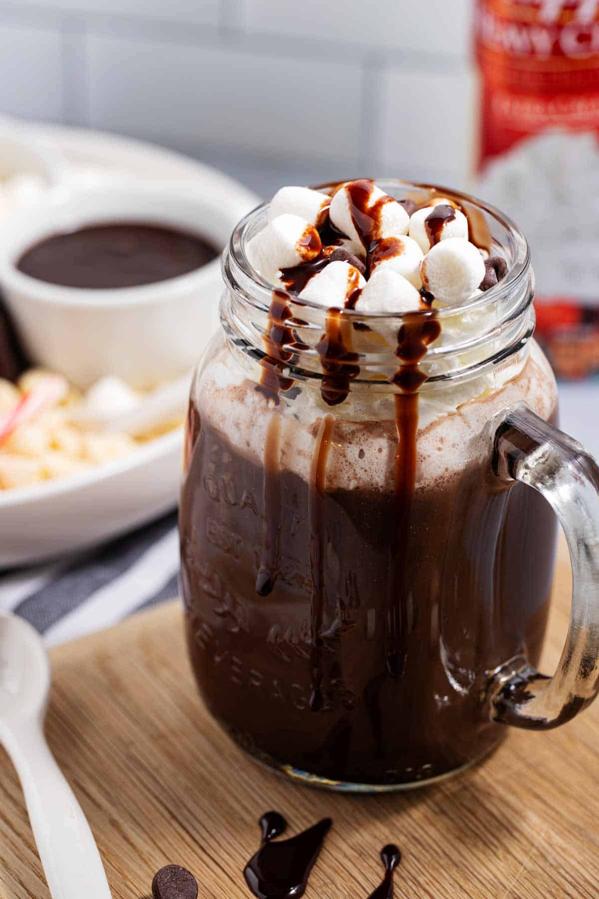 Mason jar cup filled with hot chocolate made with chocolate chips and garnished with whipped cream, marshmallows, and chocolate syrup.