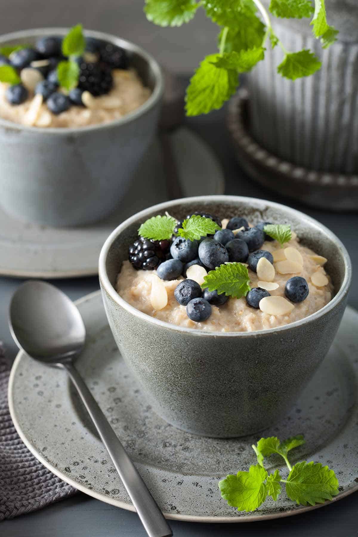 Cup of steel cut oatmeal garnished with almond slices, blueberries, blackberries and mint.