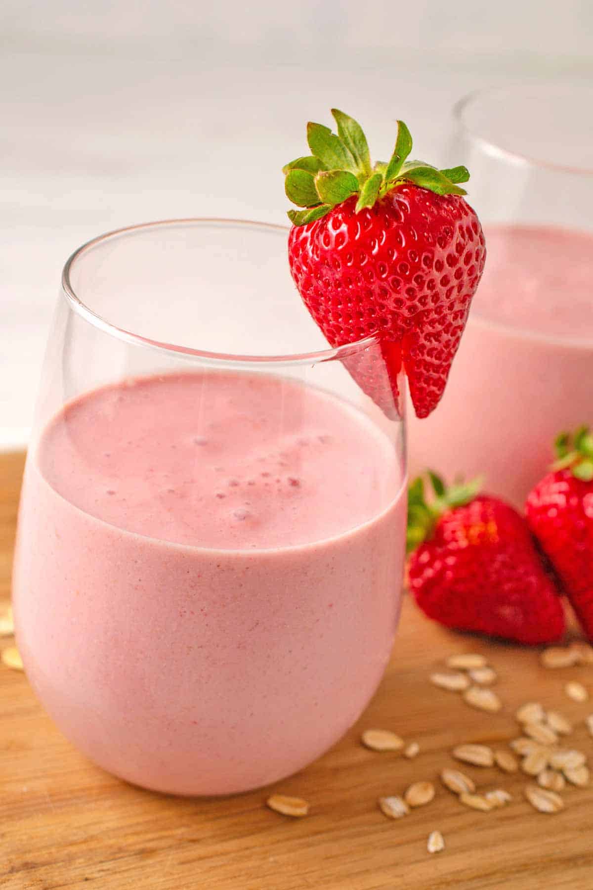 Strawberry smoothie in a glass with a strawberry on the rim.