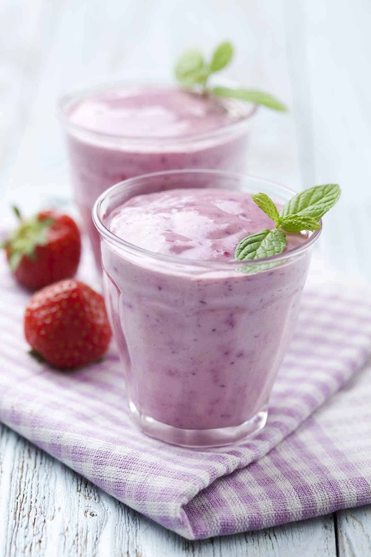 Two small glasses with strawberry yogurt with two strawberries on the side.