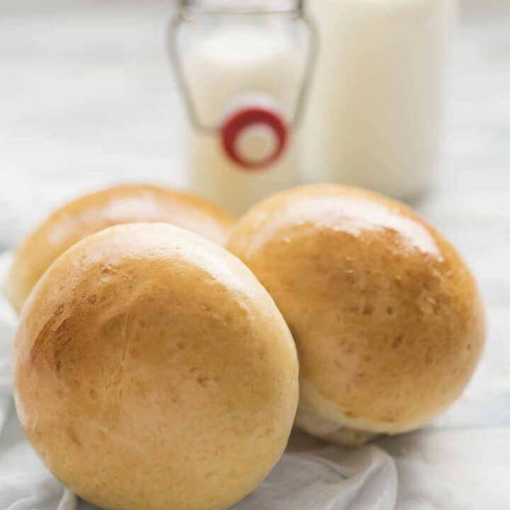 Three milk rolls with glass containers of milk in the background.