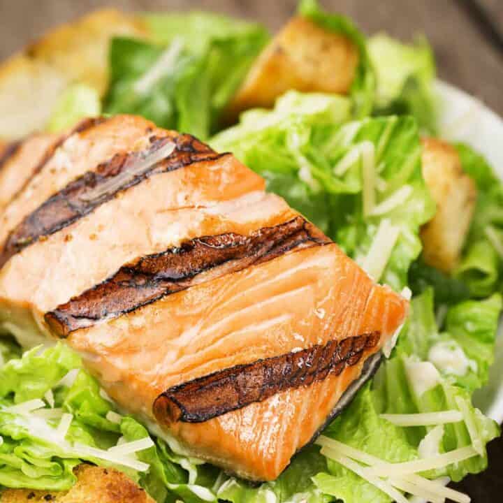 Plate of salmon Caesar salad with shredded Parmesan cheese and croutons.