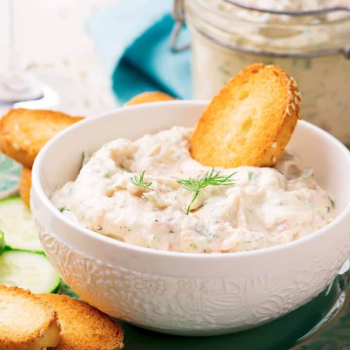 Bowl of salmon mousse with pita chips and sliced cucumbers.